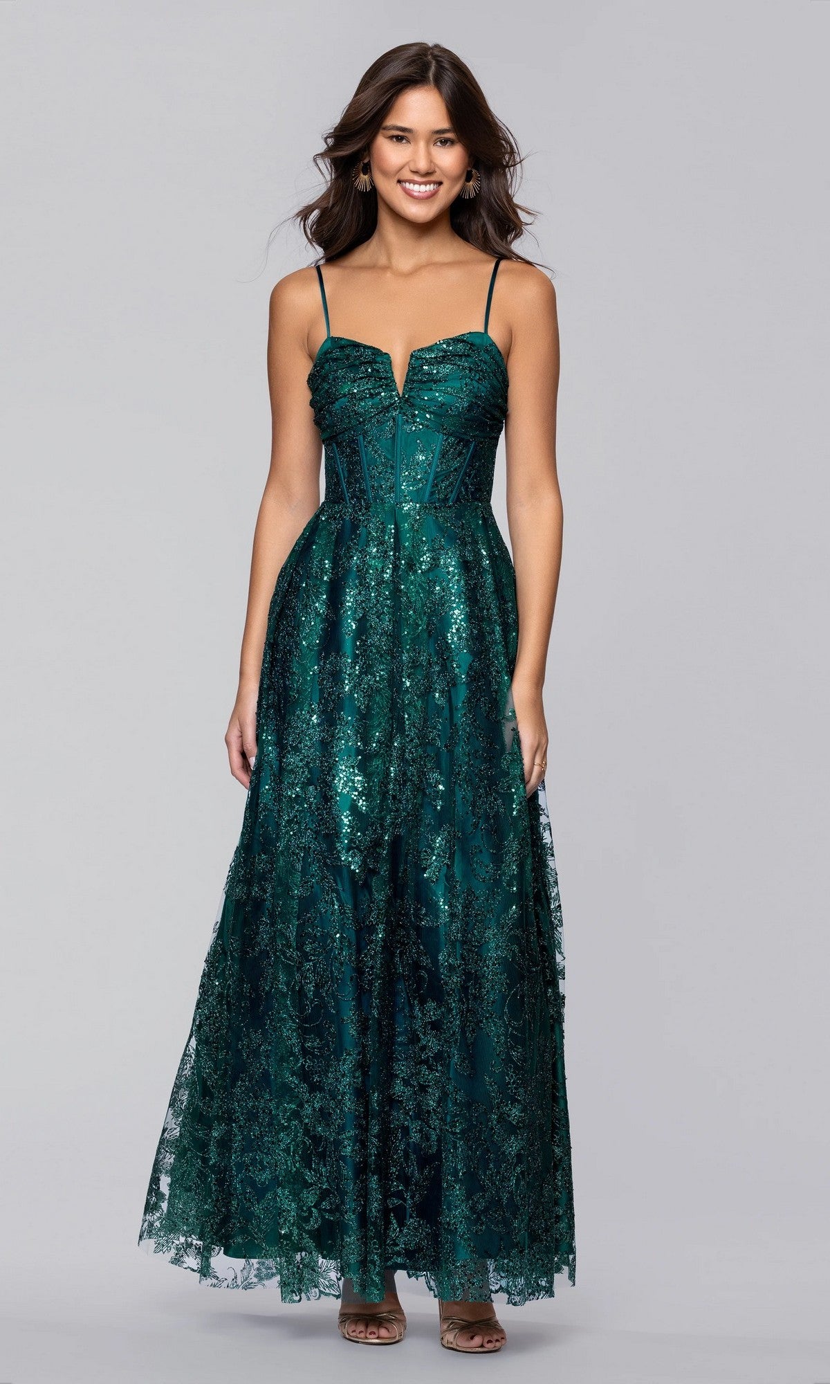 A woman wearing the Blondie Nites 5409BN long prom dress in teal, featuring a sleeveless sequin bodice, thin straps, and an elegant a-line floor-length skirt, stands smiling against a plain gray background.